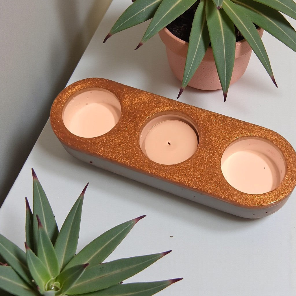 Three candle holders in a decorative holder with plants on a white surface