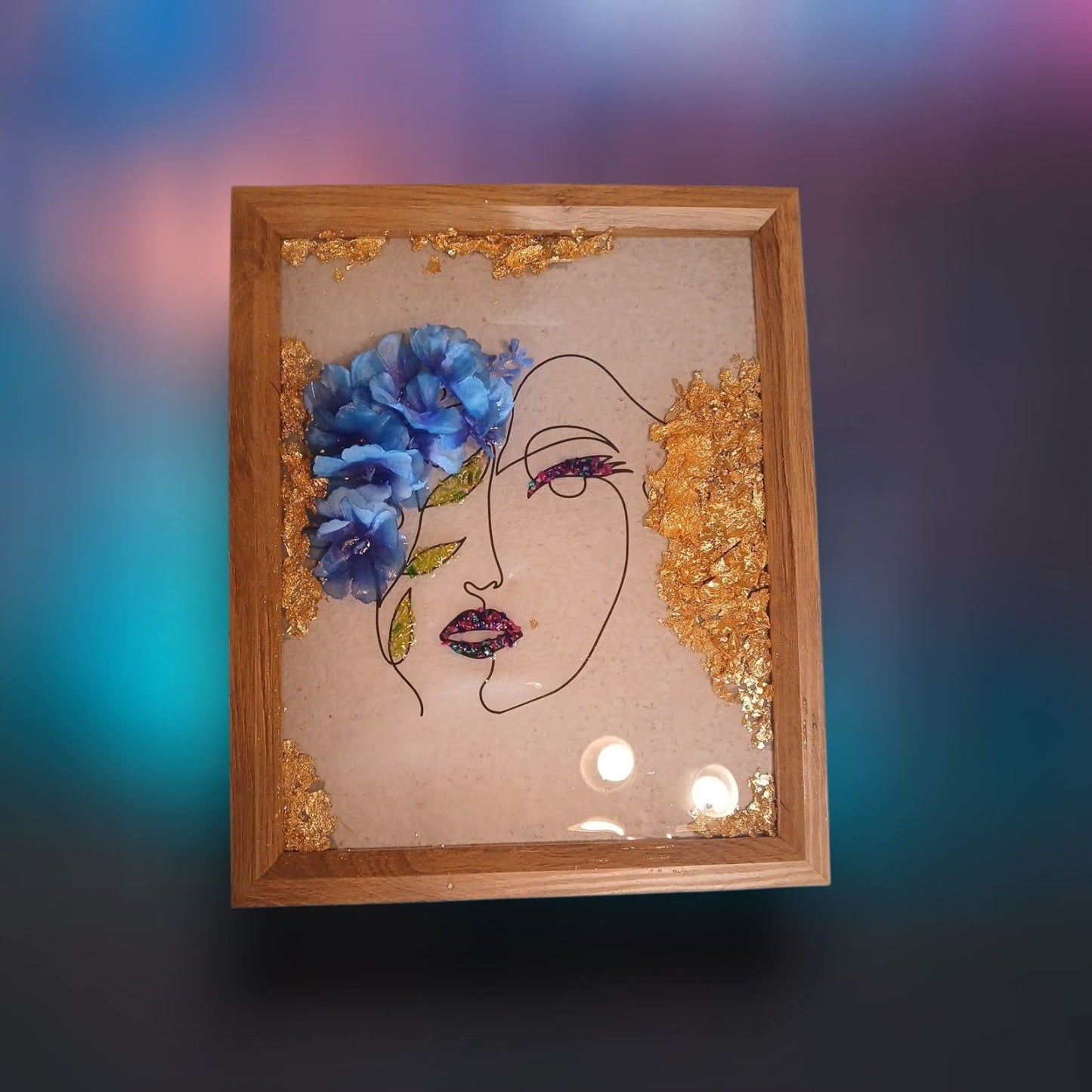 Framed artwork with a face design and blue flowers on a gradient background