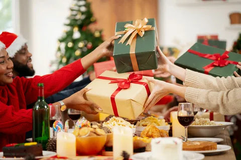 People exchanging gifts at a festive holiday gathering with Christmas decorations.