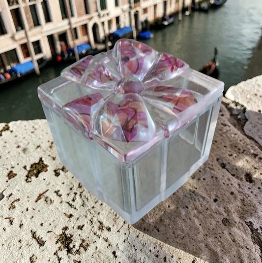 Decorative glass block with pink floral pattern on a stone surface by a canal.