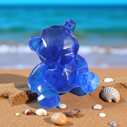 Blue glass bear figurine on a sandy beach with ocean in the background