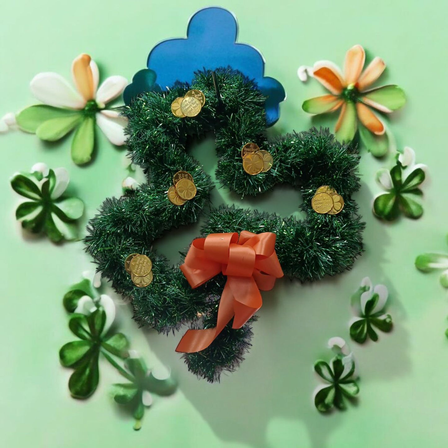 Decorative wreath with an orange bow surrounded by shamrock-shaped flowers on a light green background
