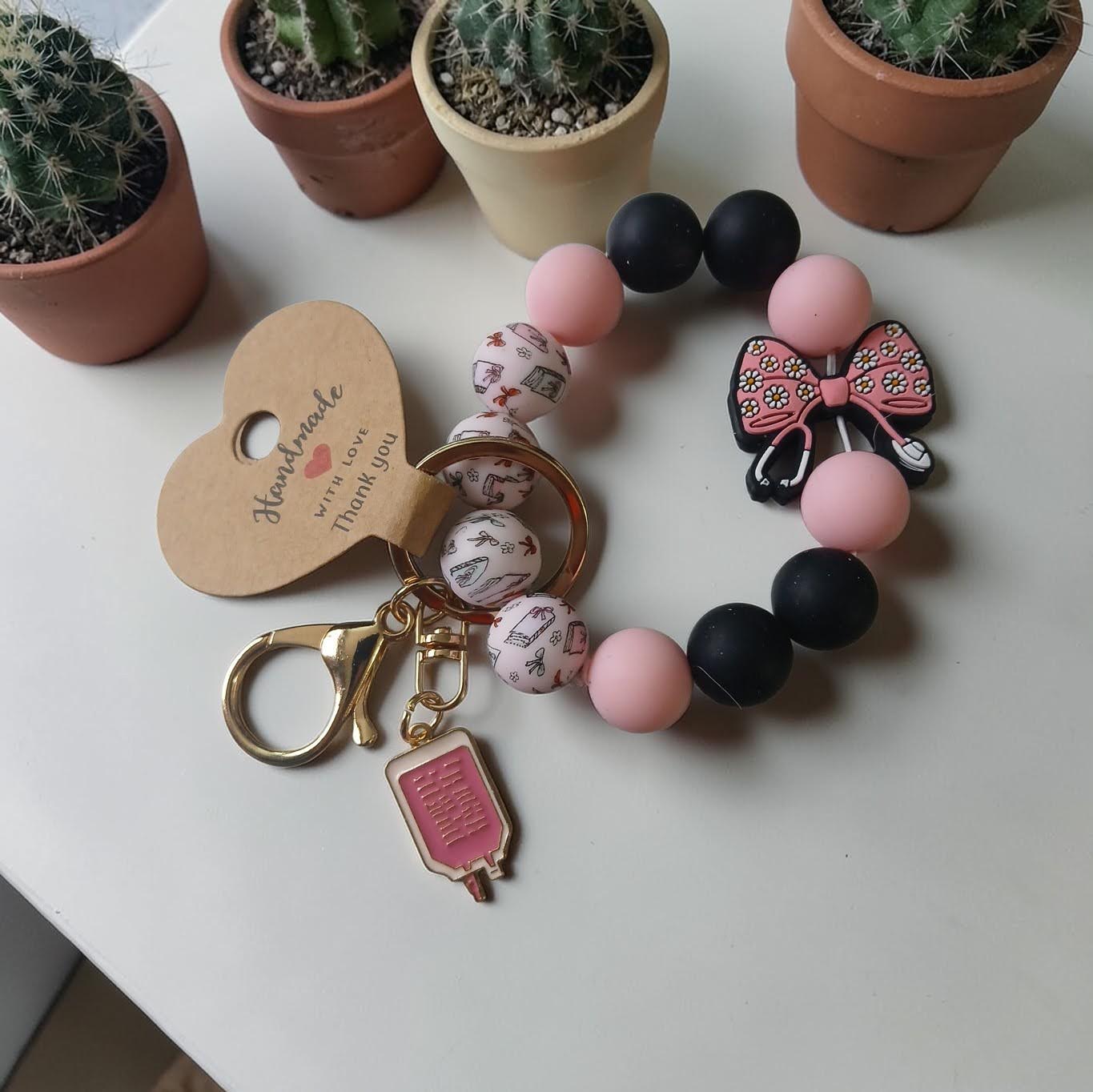 Bracelet with pink and black beads and keychain on a white surface with potted cacti in the background.