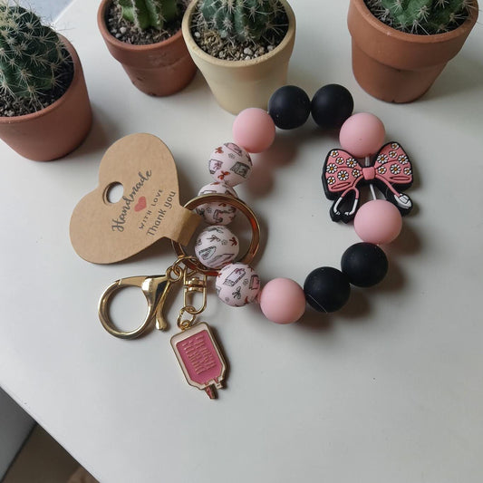 Bracelet with pink and black beads and keychain on a white surface with potted cacti in the background.