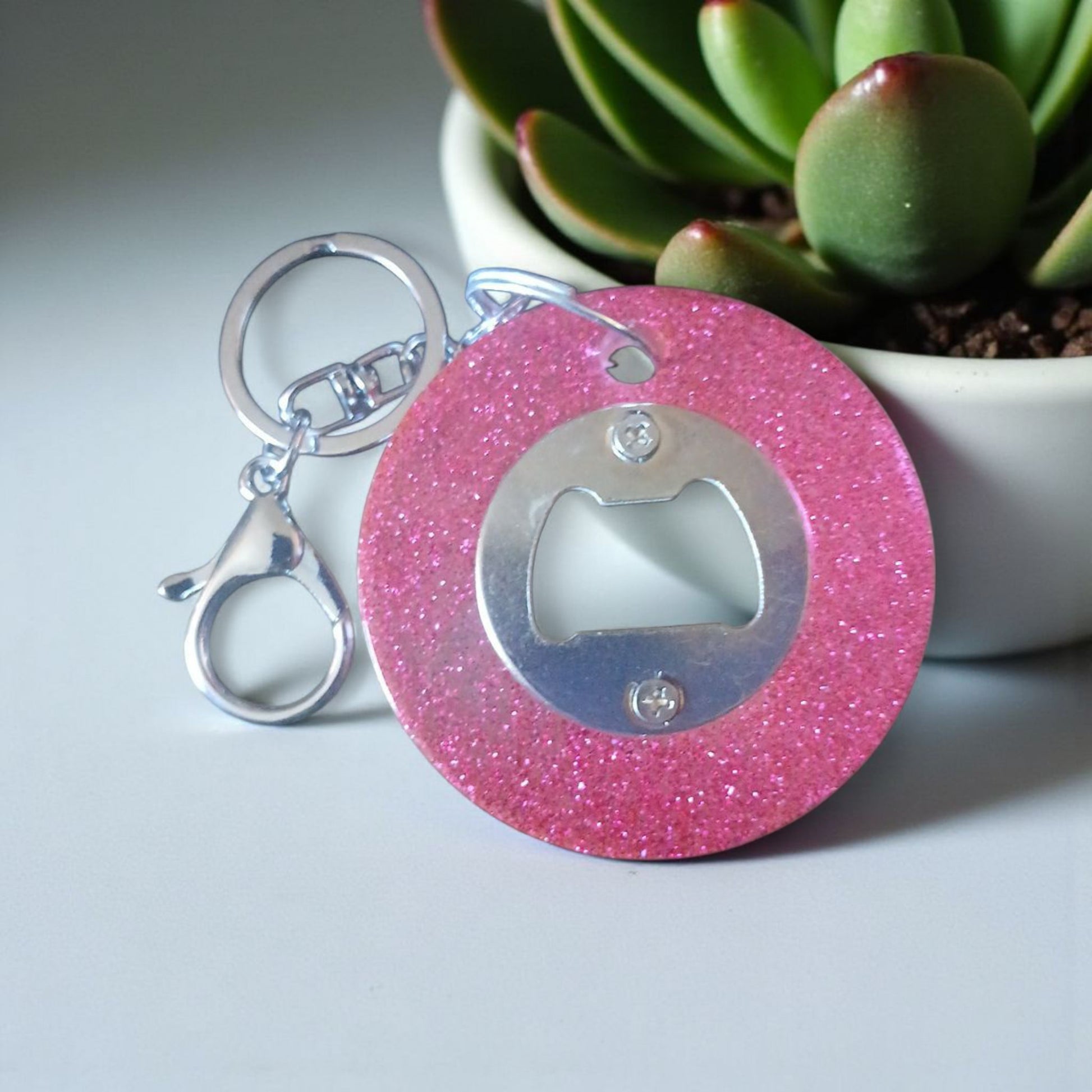 Pink glittery bottle opener keychain with a plant in the background