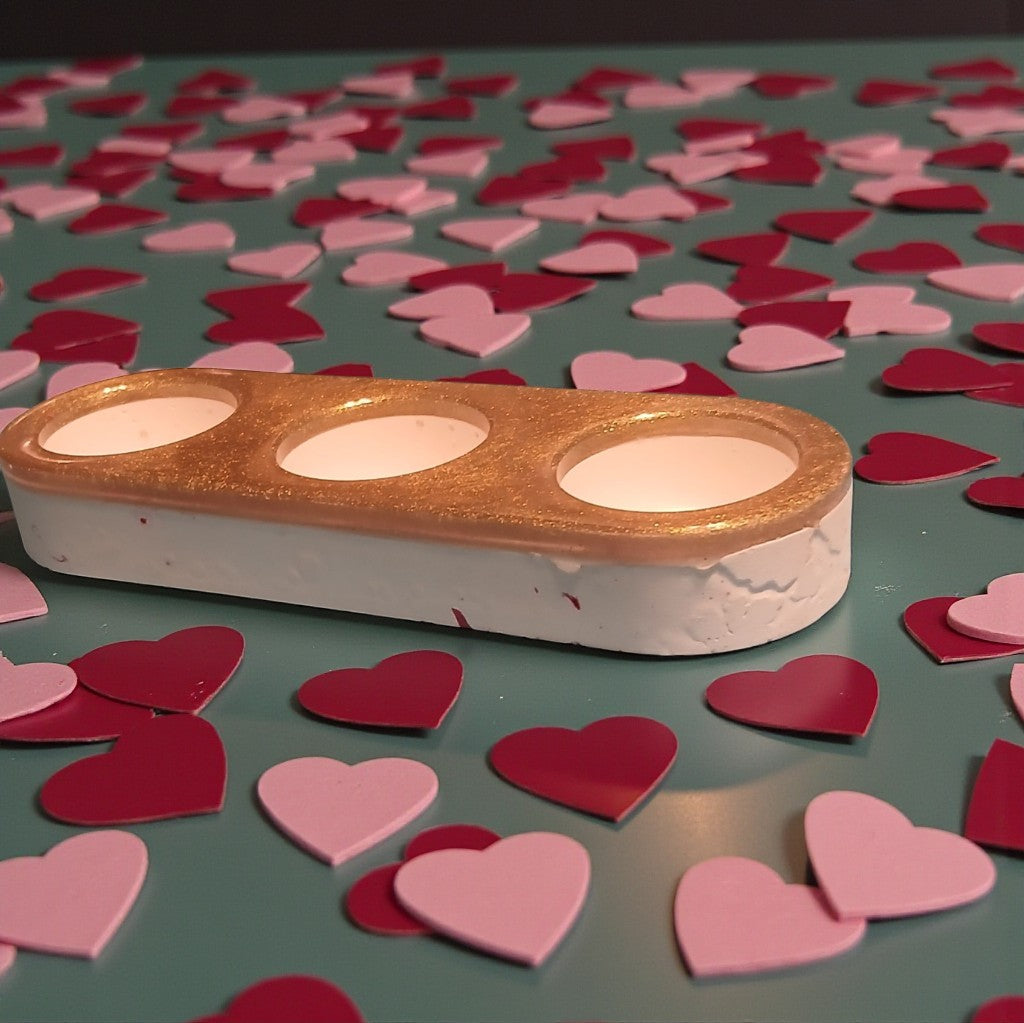 Gold and white candle holder with heart-shaped candles on a green surface with scattered pink and red heart-shaped candles.