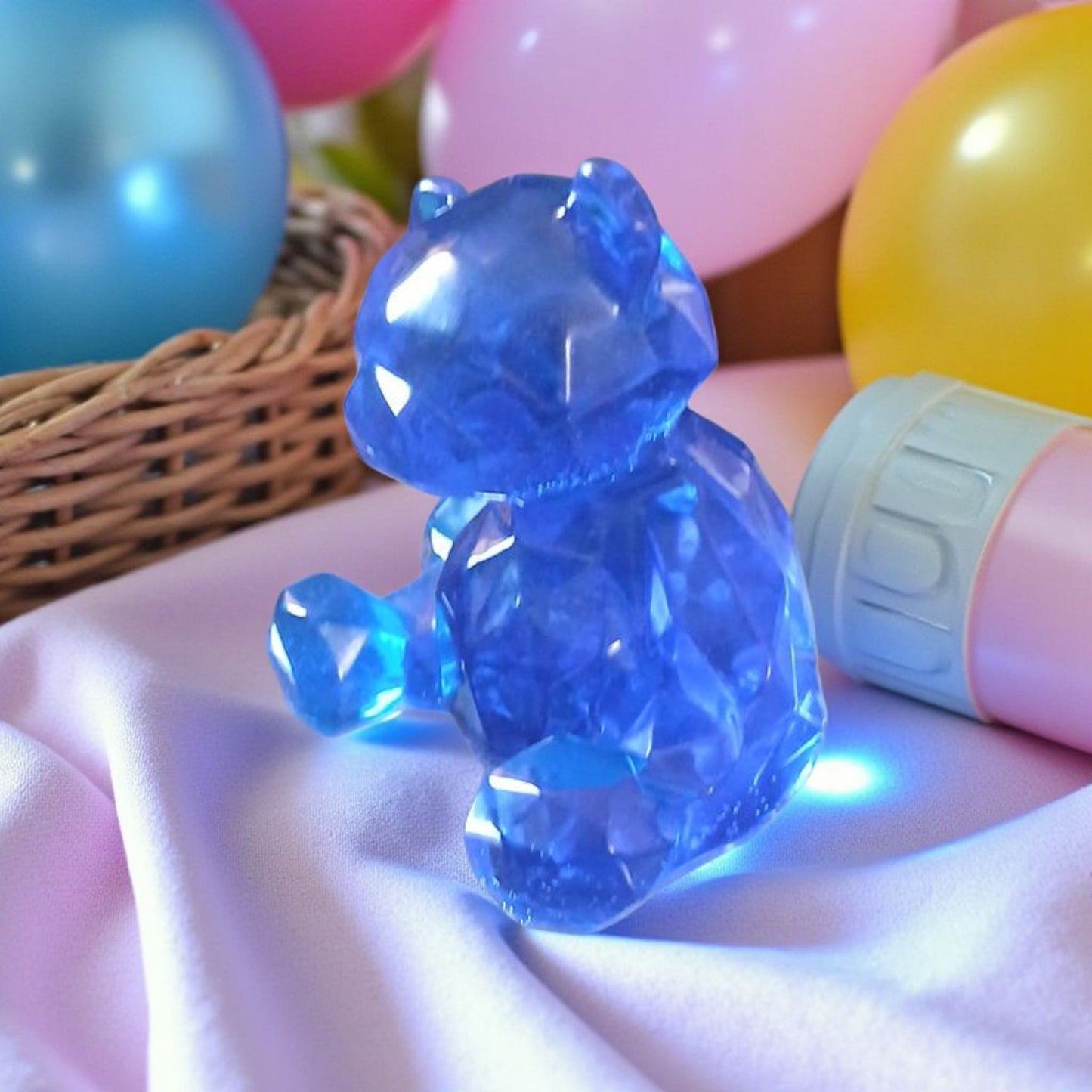 Blue crystal bear figurine on a pink surface with colorful balloons in the background