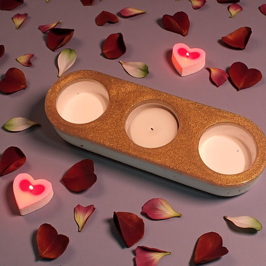 Three-wick candle holder with heart-shaped candles on a surface with red and pink petals.