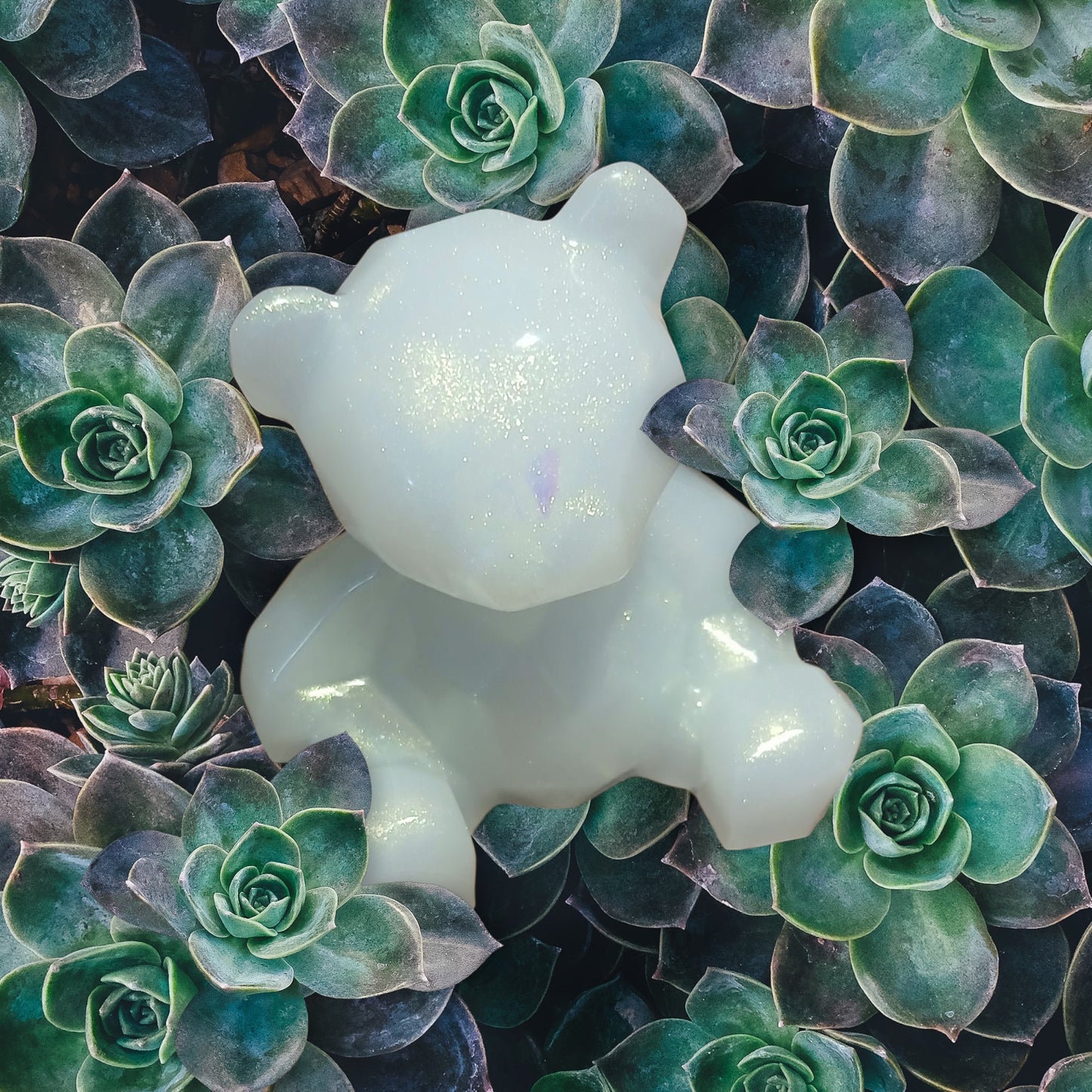 White cat-shaped candle among green succulents