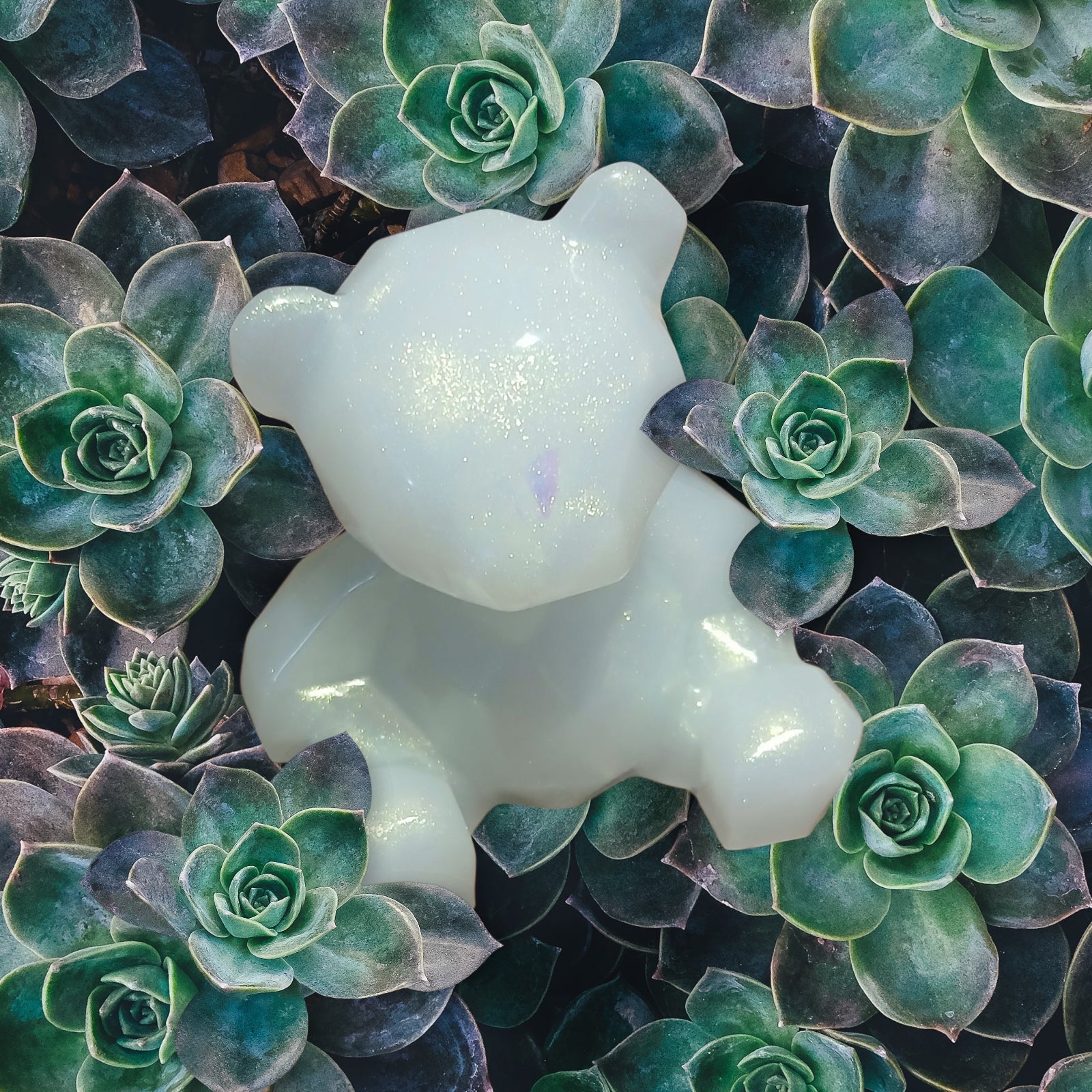 White cat-shaped candle among green succulents