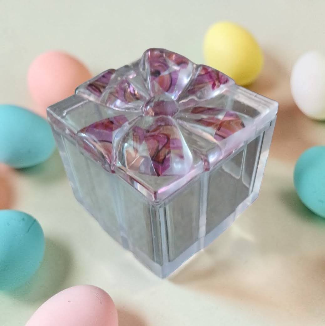 Clear square mold with colorful contents surrounded by pastel-colored balls on a light background