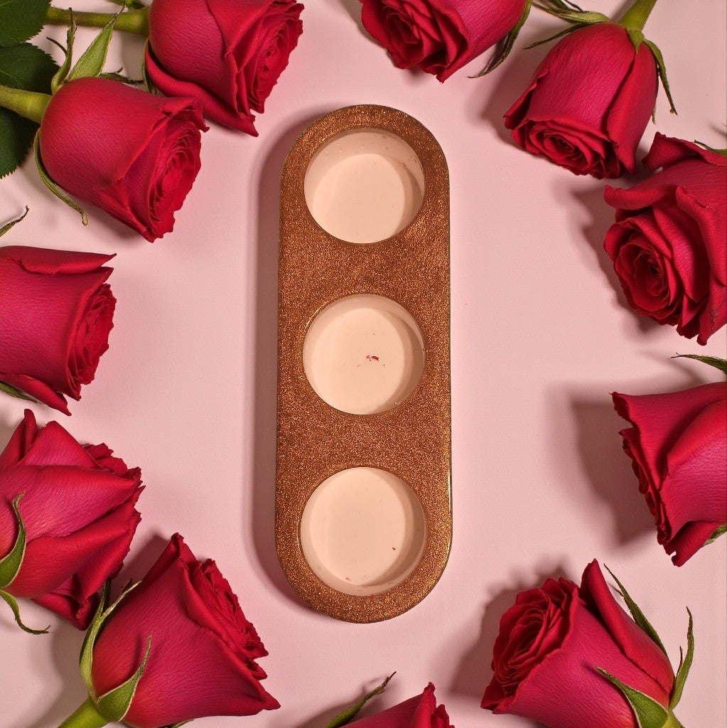 Three round candles in a decorative holder surrounded by red roses on a pink background