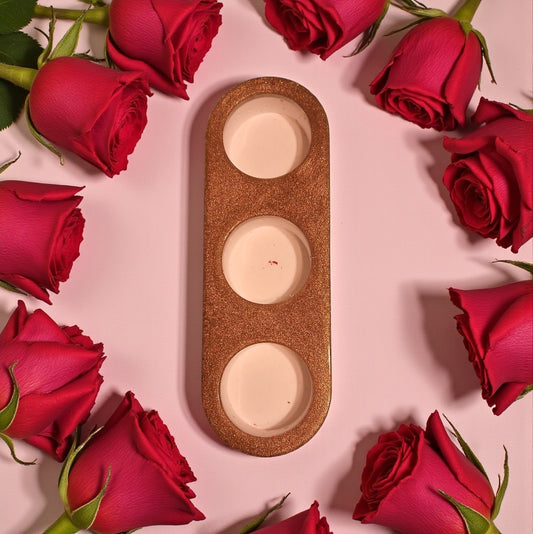 Three round candles in a decorative holder surrounded by red roses on a pink background